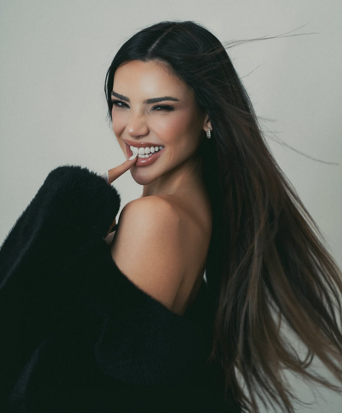 Eileen León biting her fingertip and winking over a bare shoulder