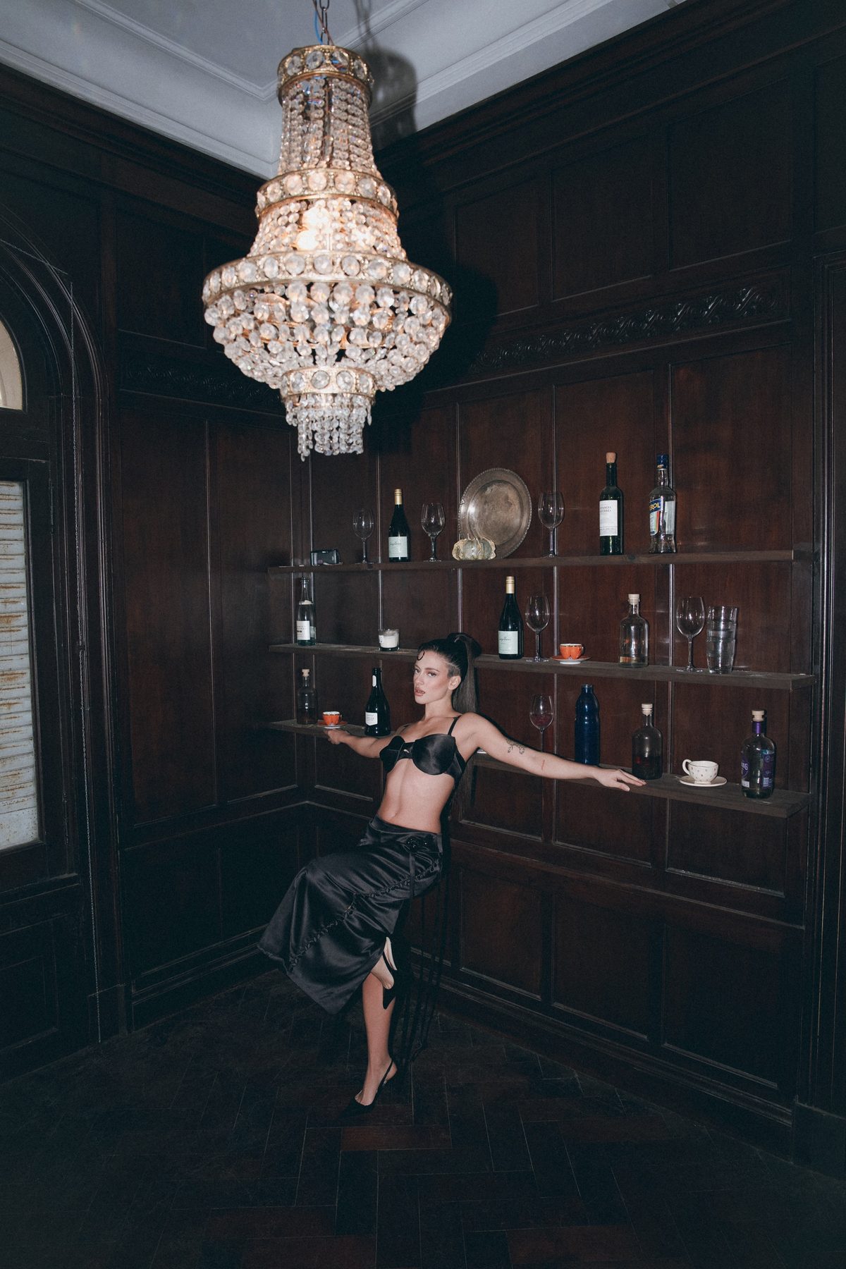 Greta Cozzolino in black satin under a crystal chandelier in a wood-panelled room