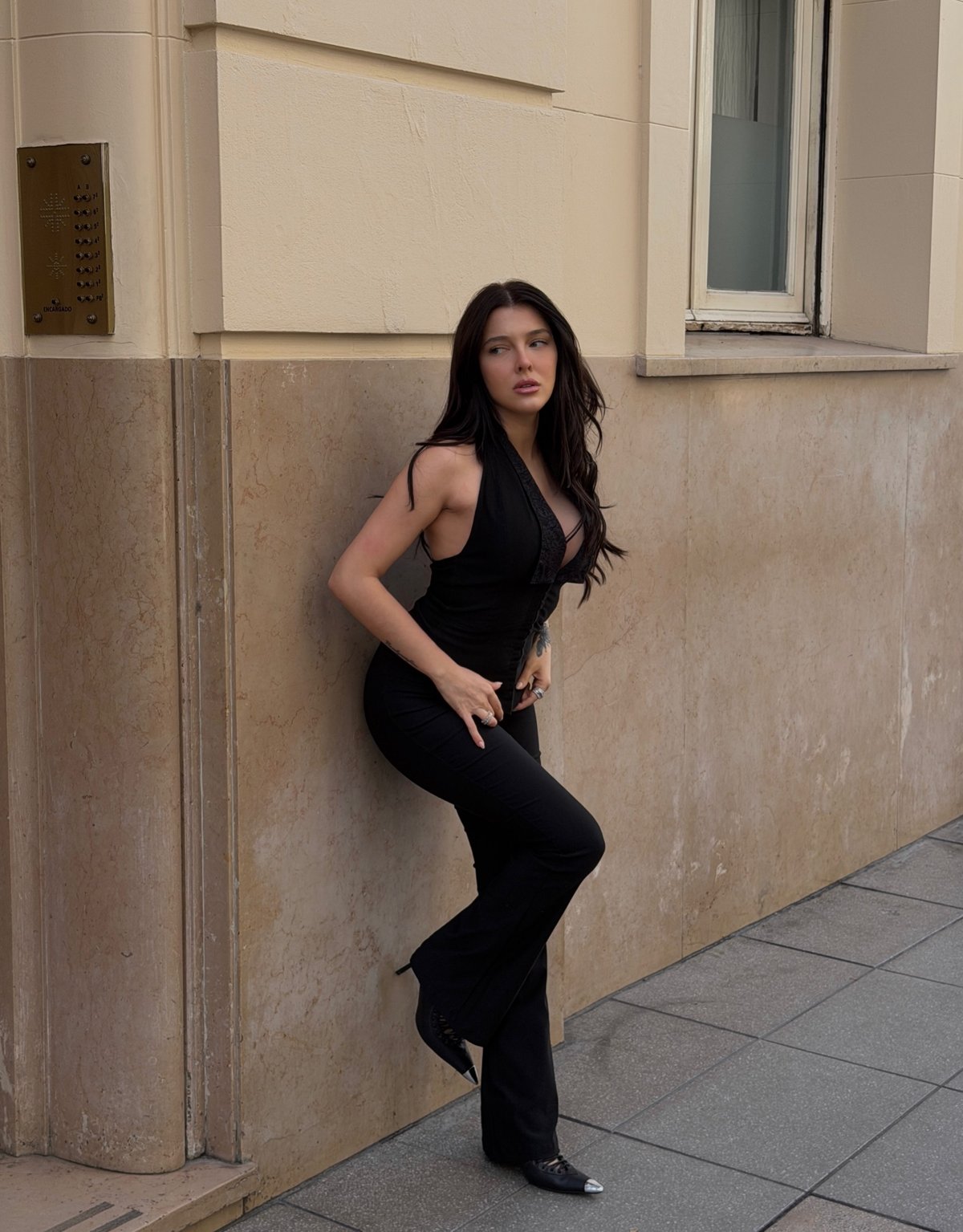 Model in a black halter and flared trousers leaning on a sunlit façade
