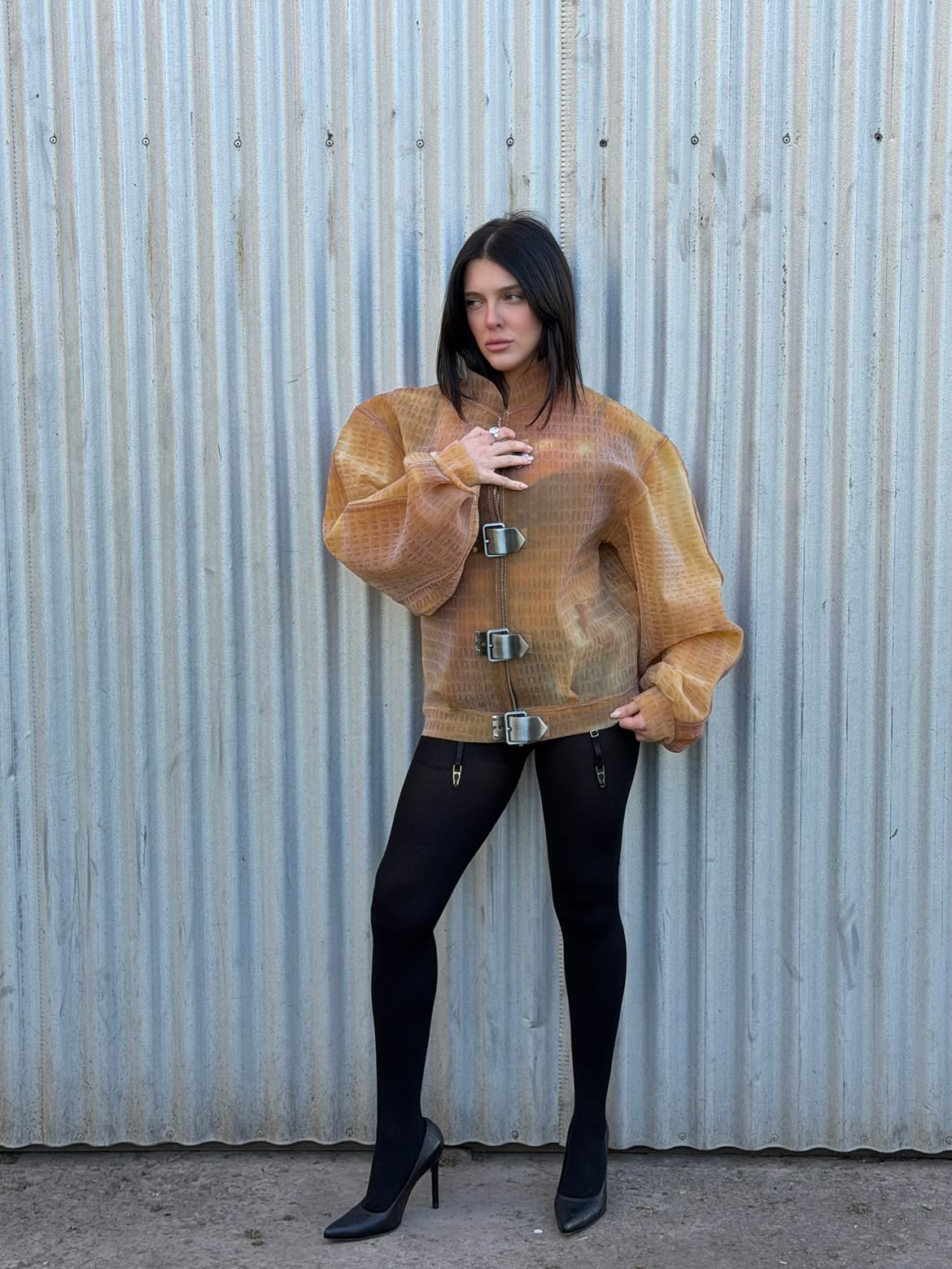 Model in a sheer croc jacket and black tights against corrugated metal