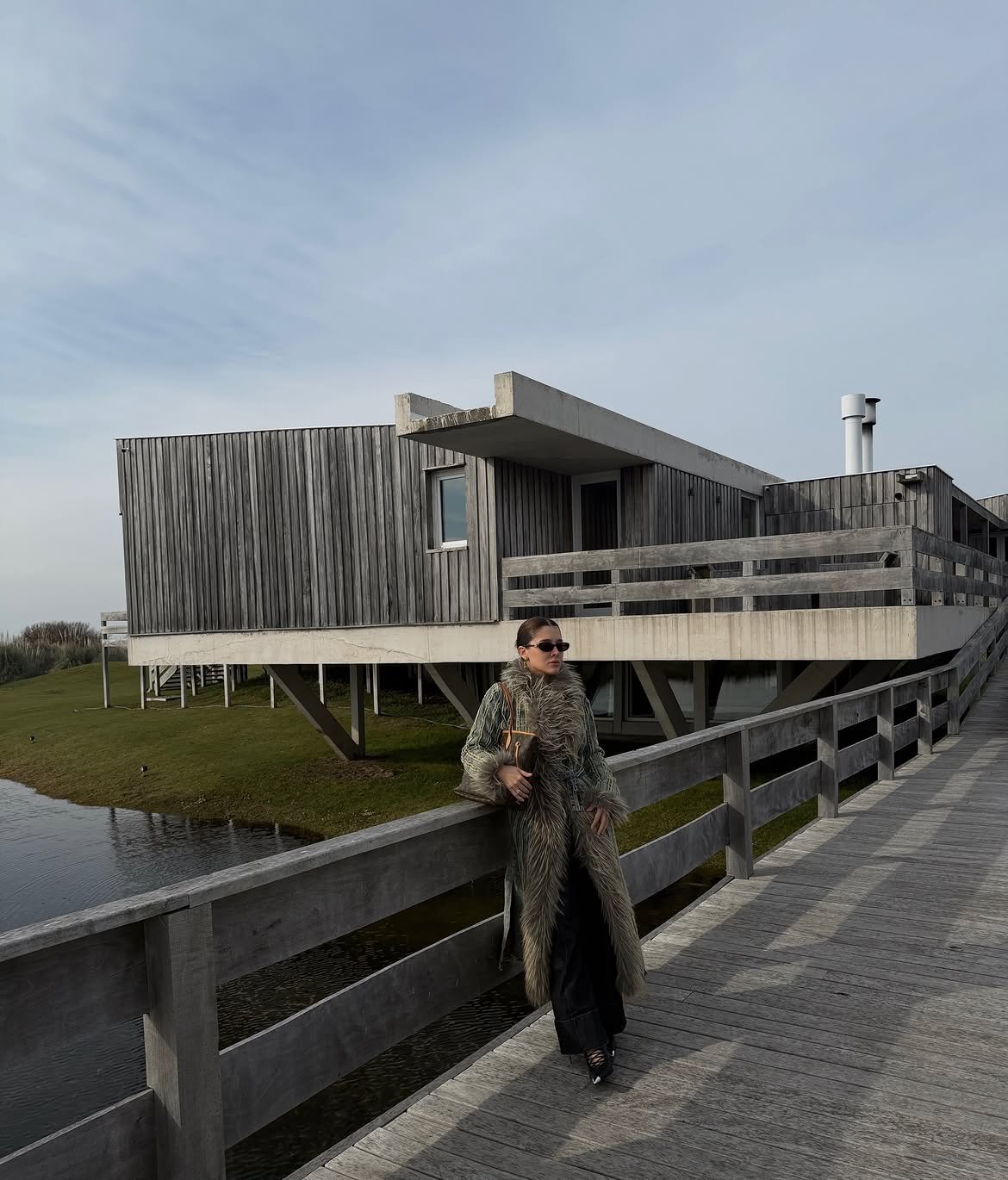 Model in a long shaggy coat on a wooden boardwalk by a modern timber house