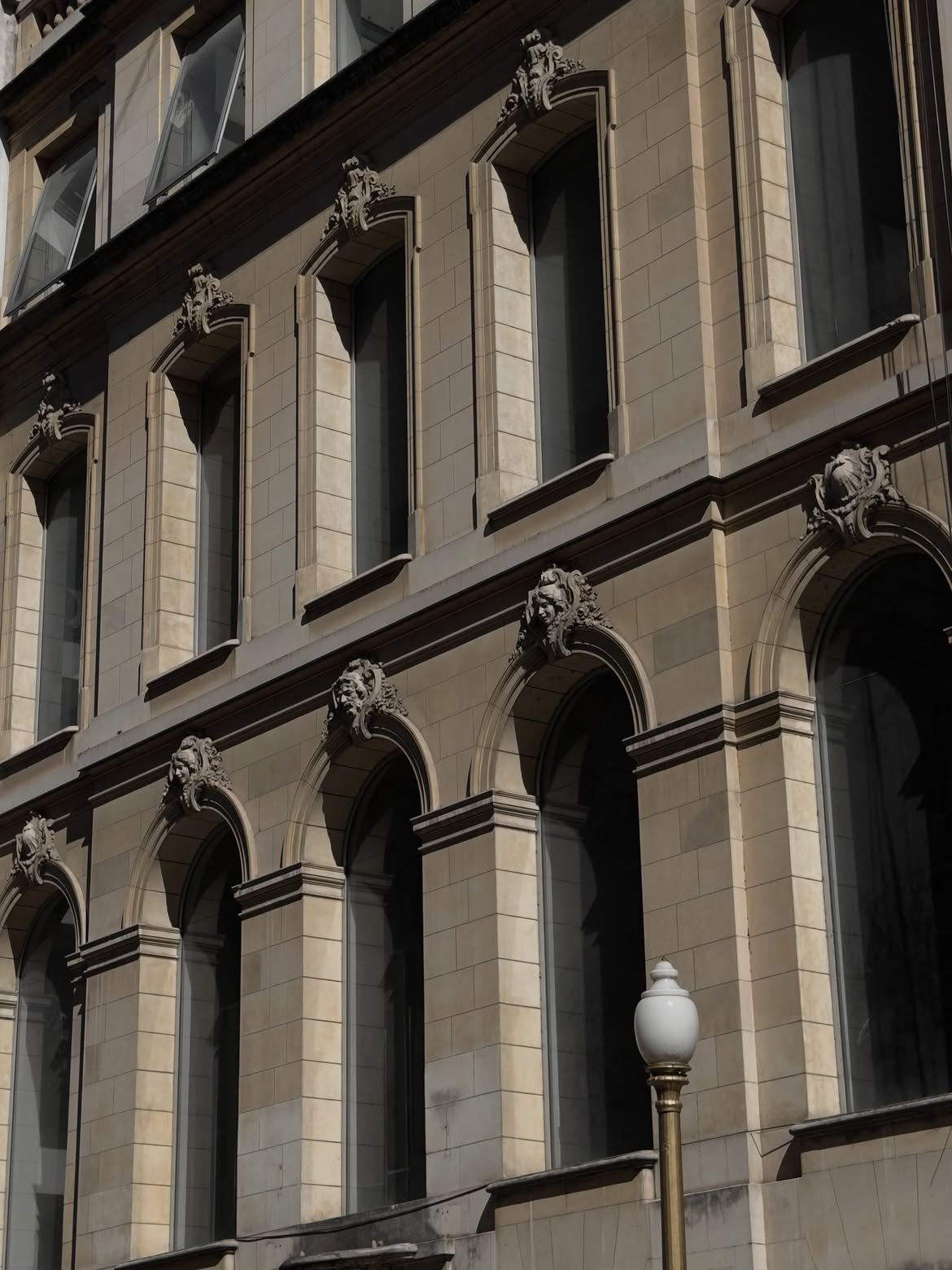 Stone façade with carved masks above arched windows and a street lamp