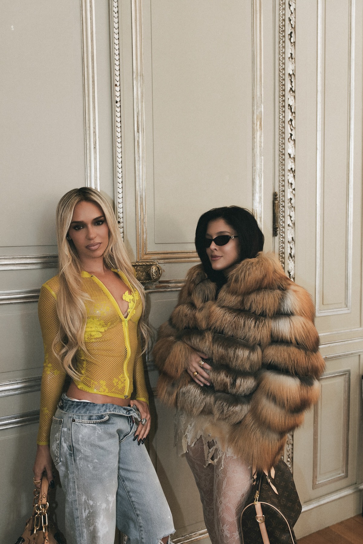 Sofía Gonet in a fox fur coat and Bad Gyal in yellow mesh against panelled boiserie
