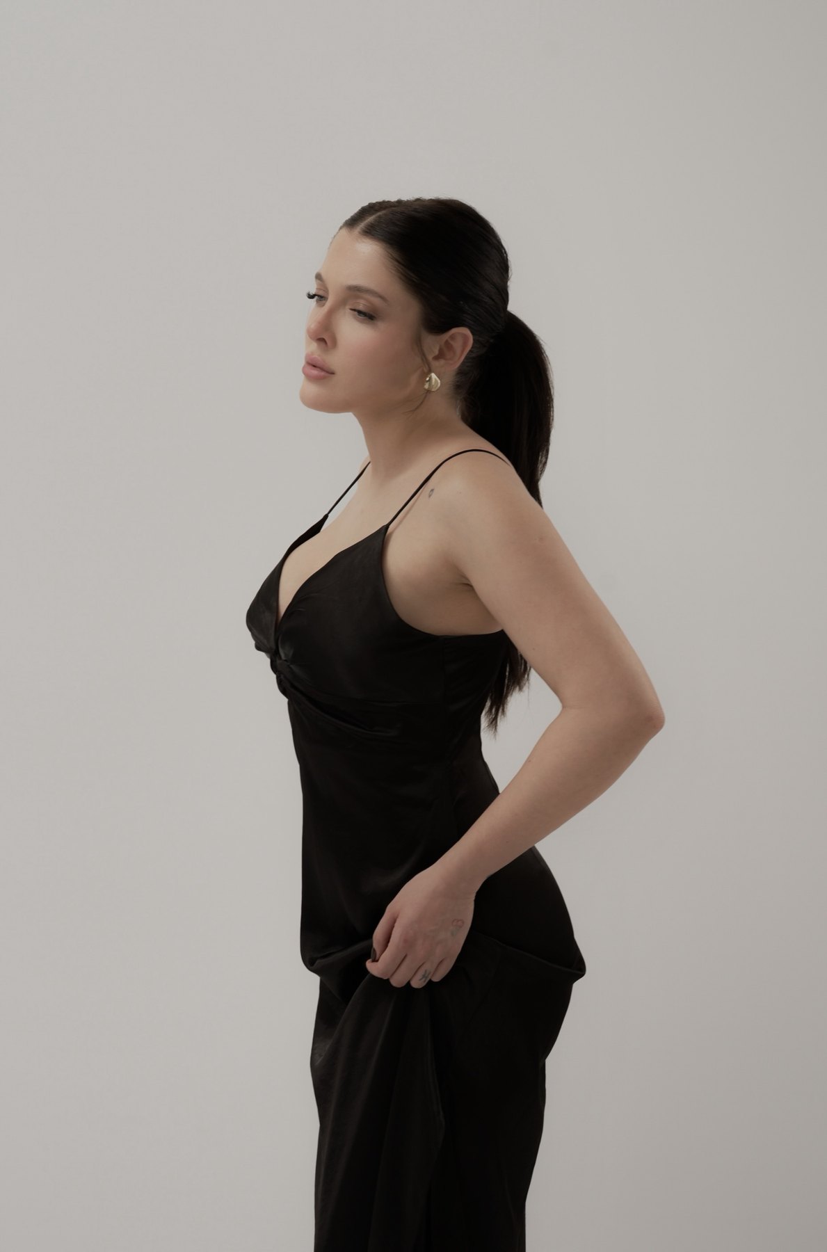Sofía Gonet in profile in a black satin slip dress, holding the skirt