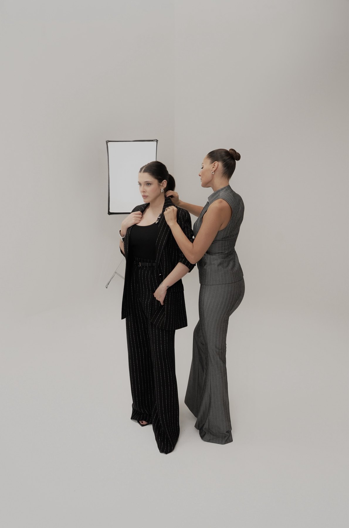 Pampita adjusting the lapel of Sofía Gonet's pinstripe suit on set