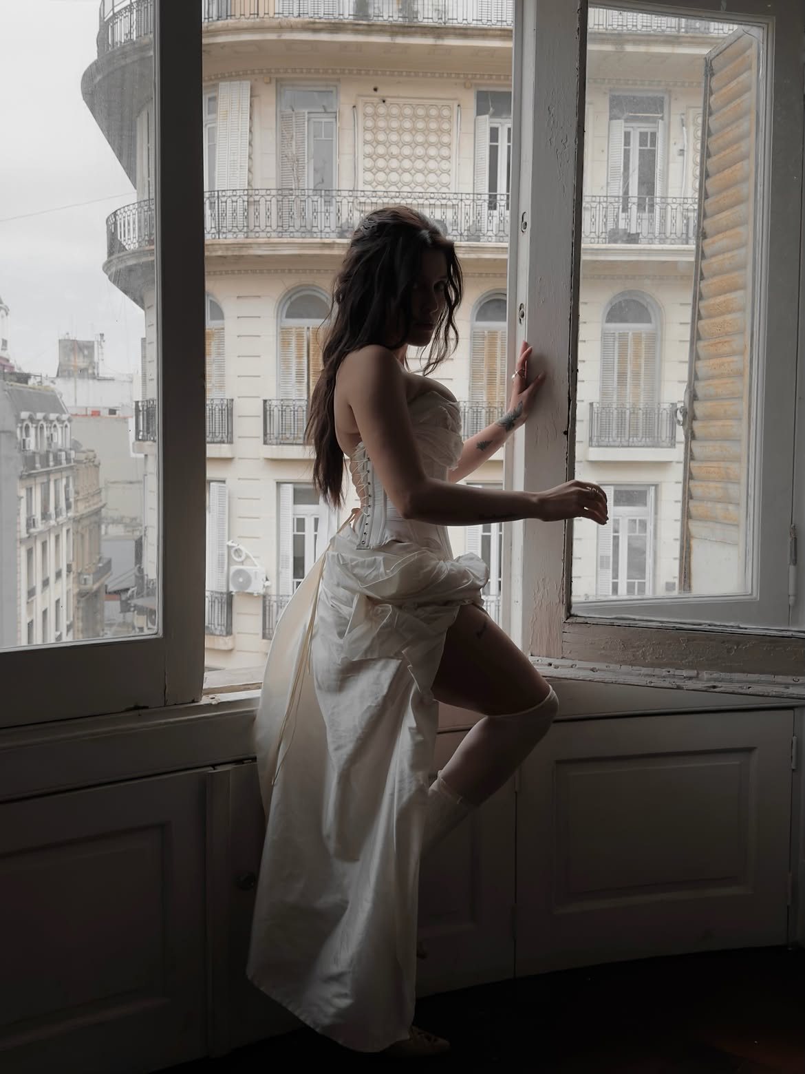 Sofía Gonet in profile at a tall window, holding the frame