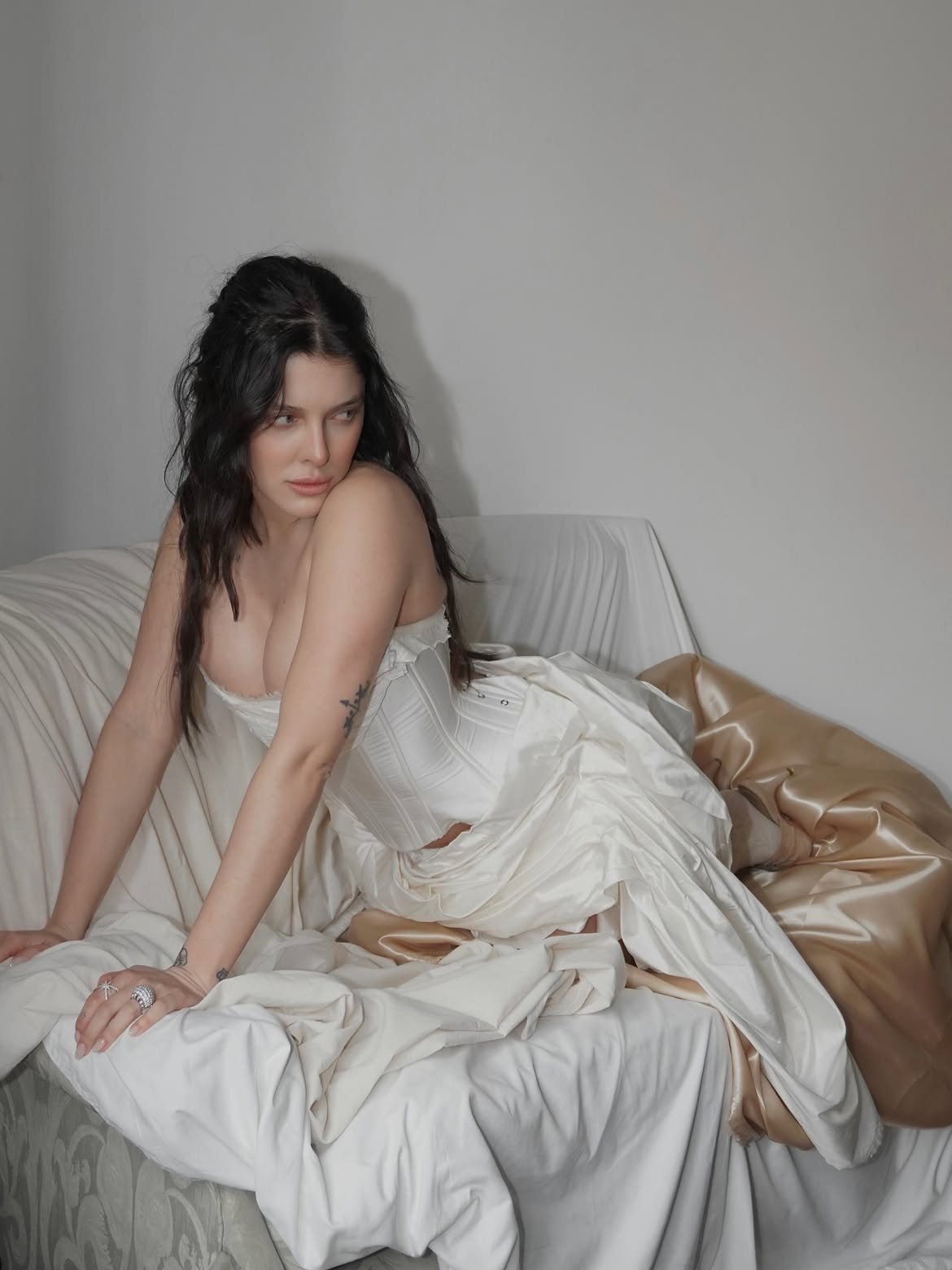 Sofía Gonet reclining on a draped sofa, glancing back