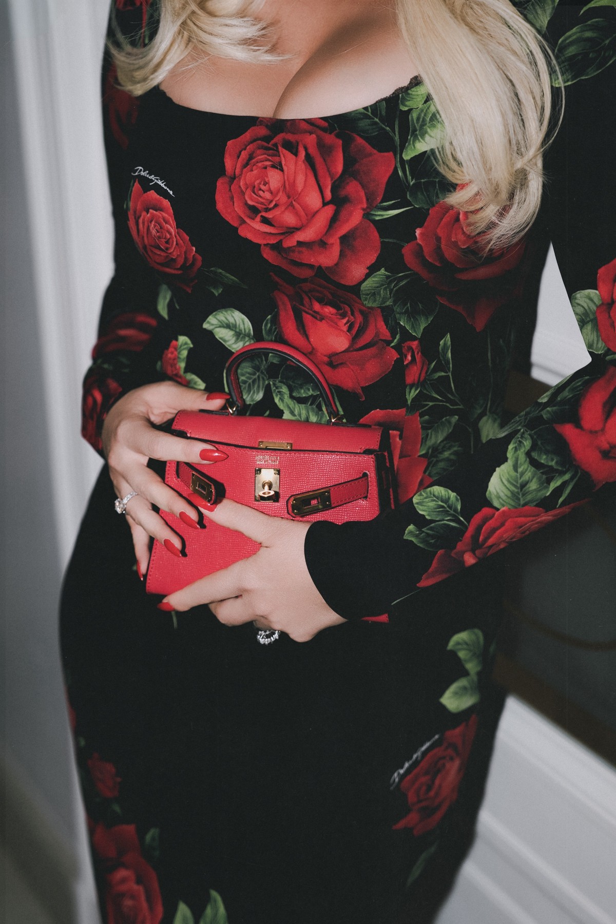 Detail of hands with red nails holding a mini red handbag against the rose-print dress