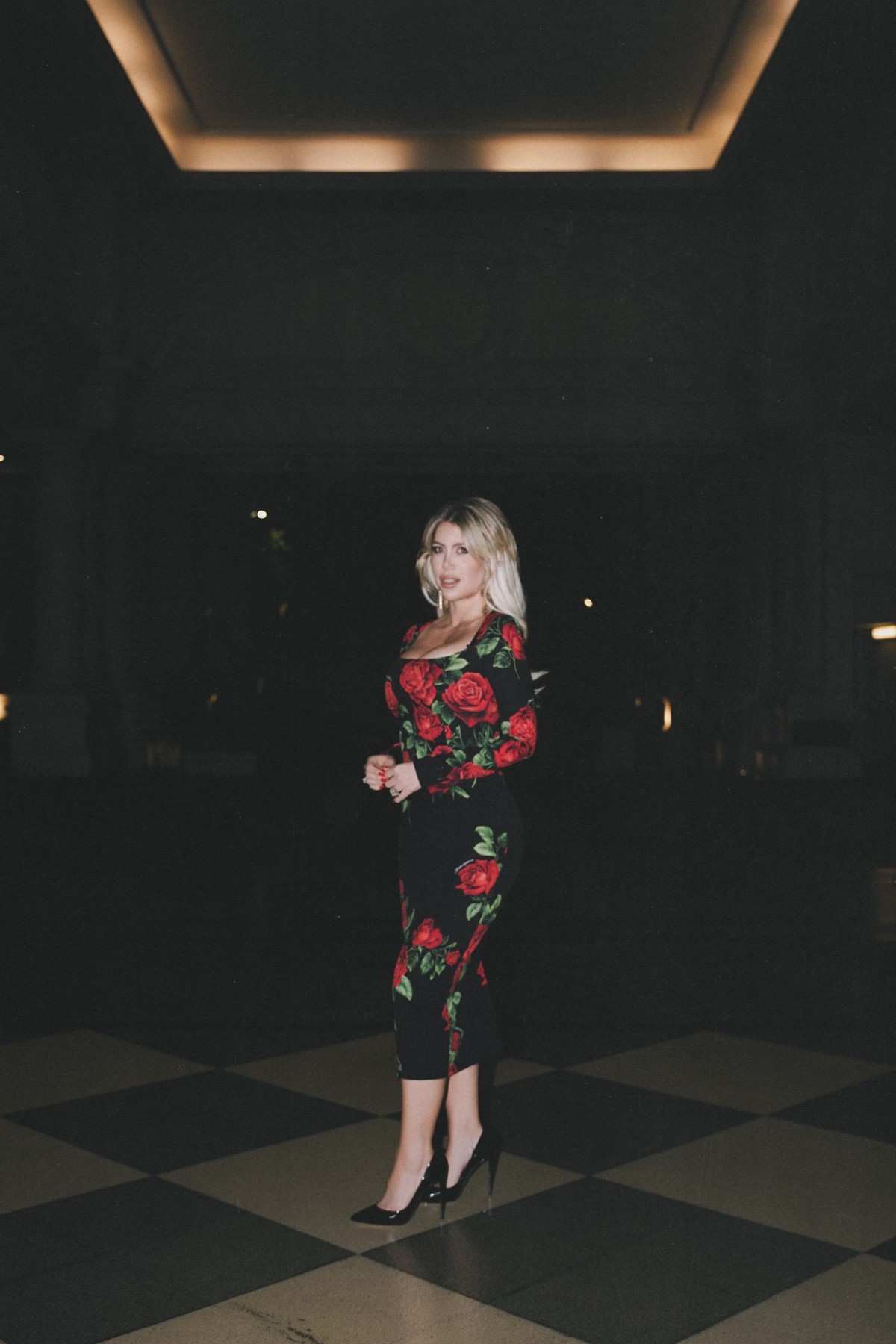 Wanda Nara on a checkered floor under a lit ceiling, shot with direct flash at night