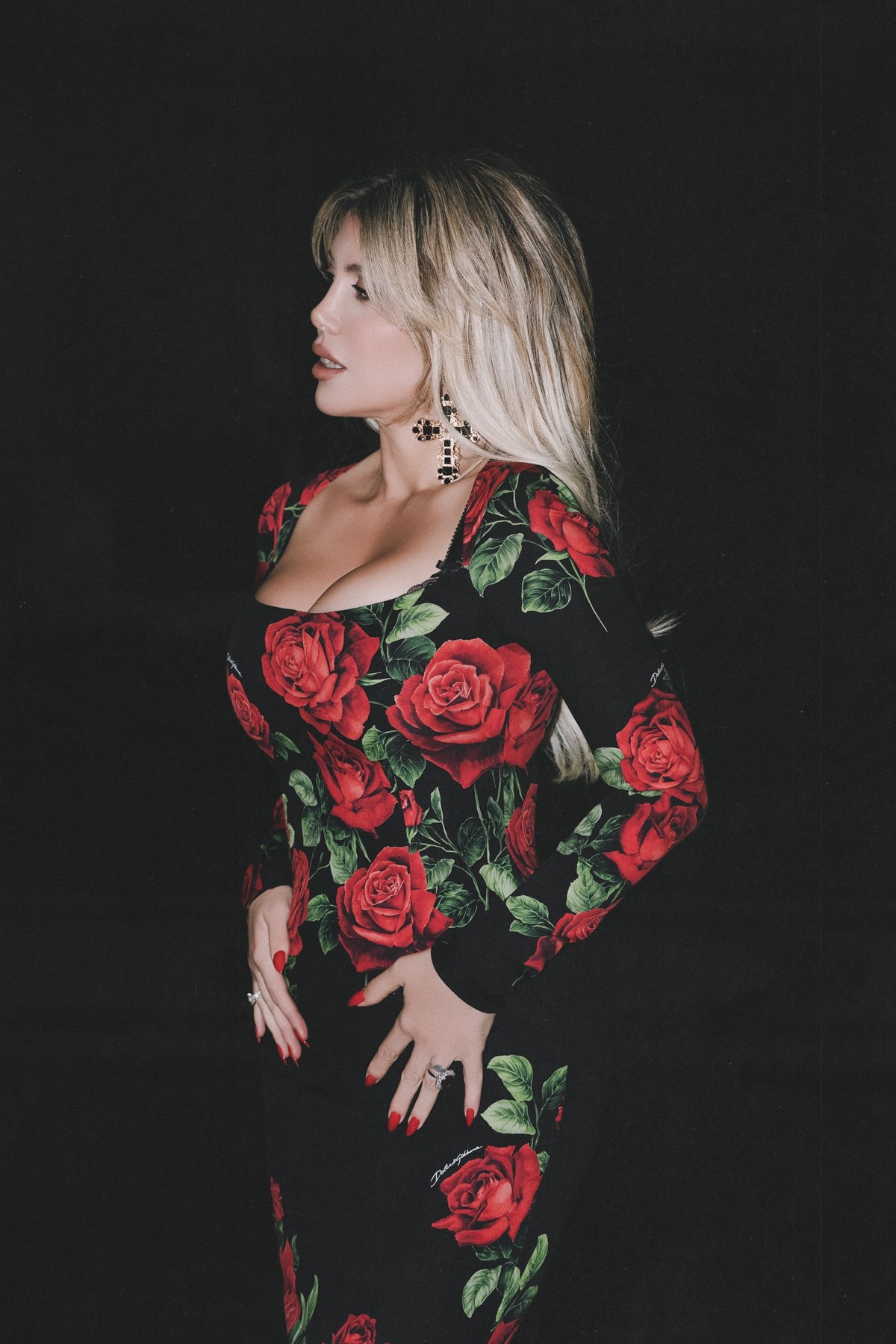 Wanda Nara in profile against black, wearing jeweled cross earrings