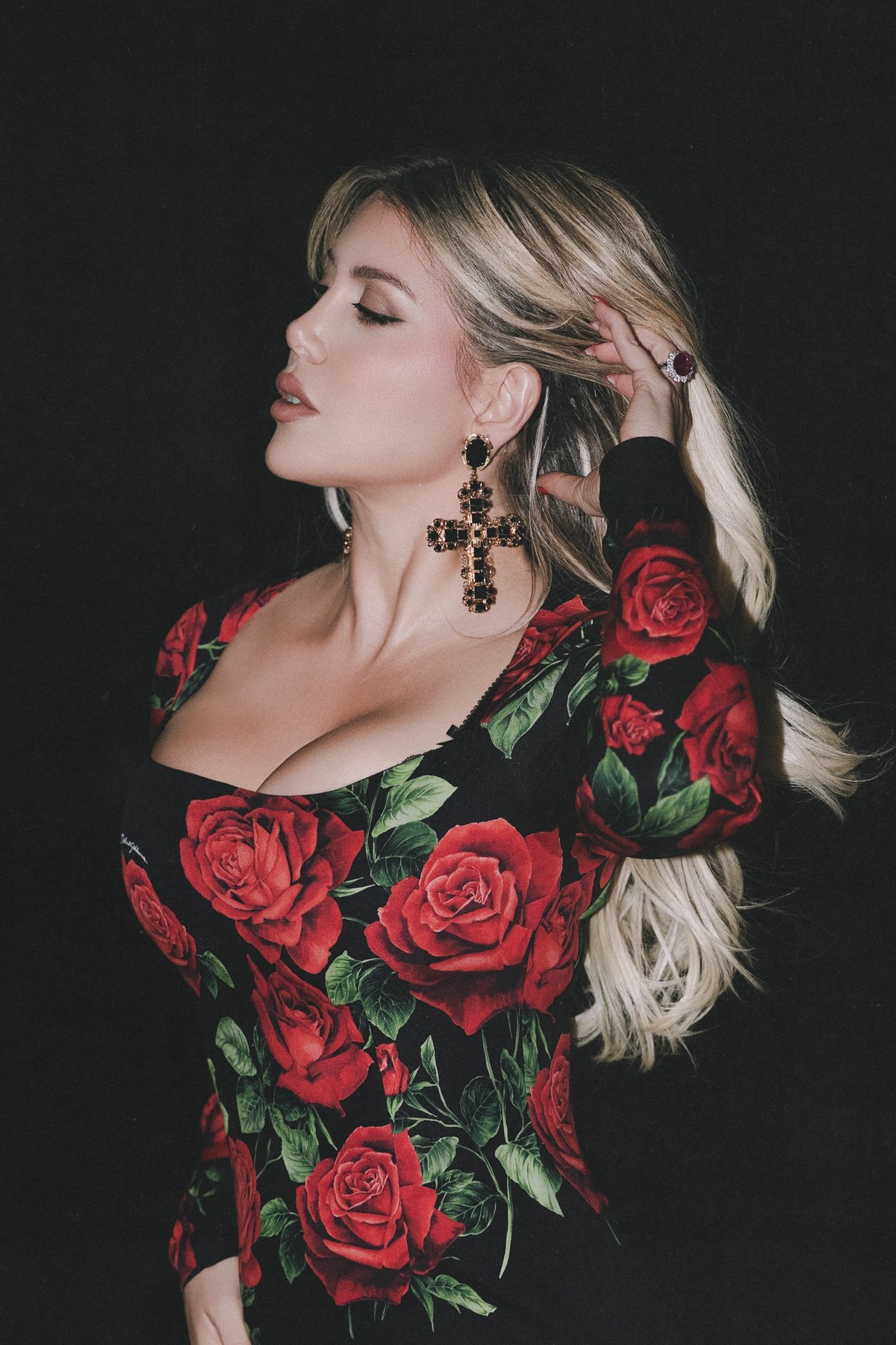 Close profile of Wanda Nara with eyes closed, hand in her hair, cross earring in focus
