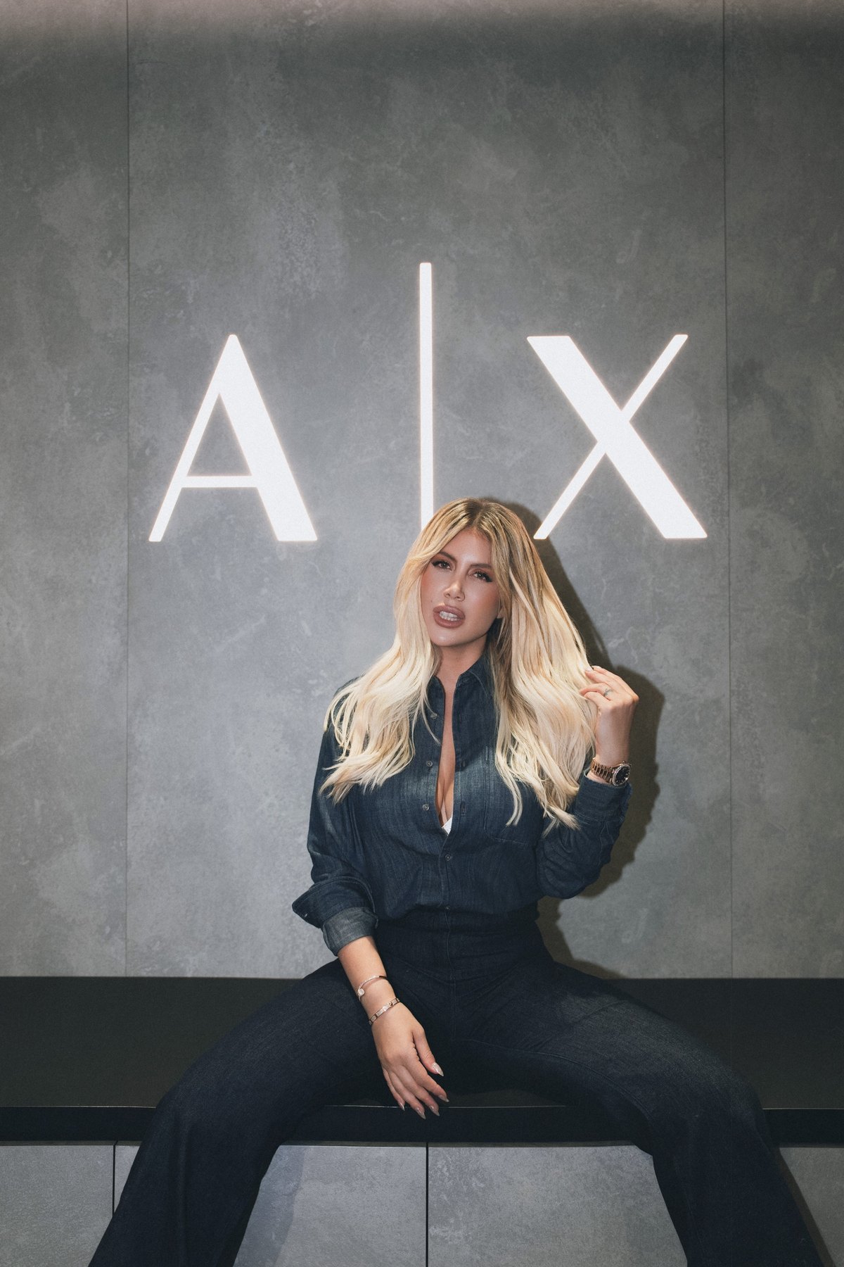 Wanda Nara playing with her hair, seated beneath the A|X logo